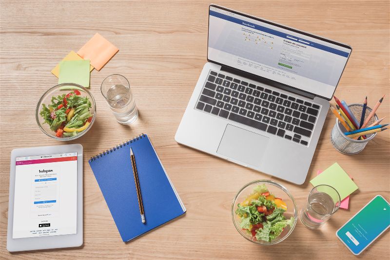 Notebook, tablet, caderneta e potinhos de salada sobre uma mesa