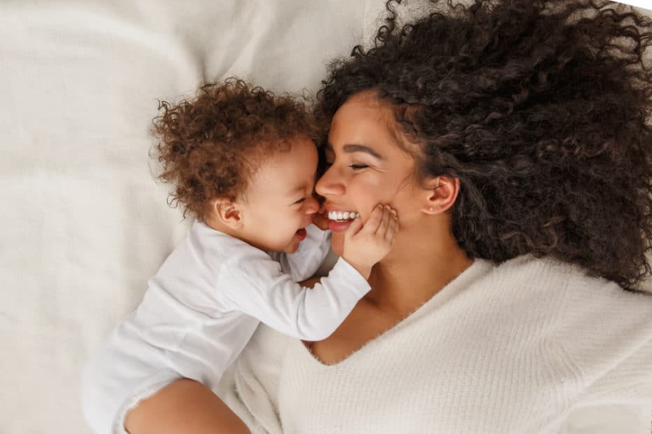 vitamina para gestante com ômega 3. Mãe e bebê deitados na cama juntos e sorrindo.