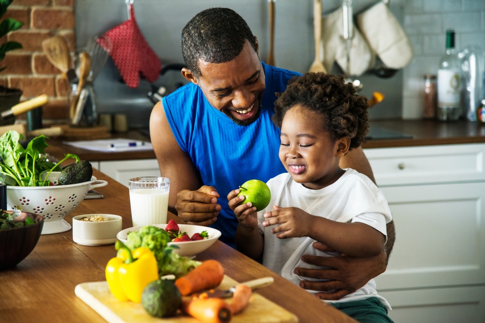 Vitaminas que aumentam a imunidade. Pai e filho se alimentando de forma saudável, em rente a uma mesa com frutas e legumes.