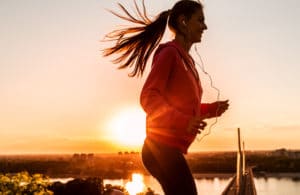 Vitaminas que aumentam a imunidade. Mulher correndo com o pôr do sol ao fundo.