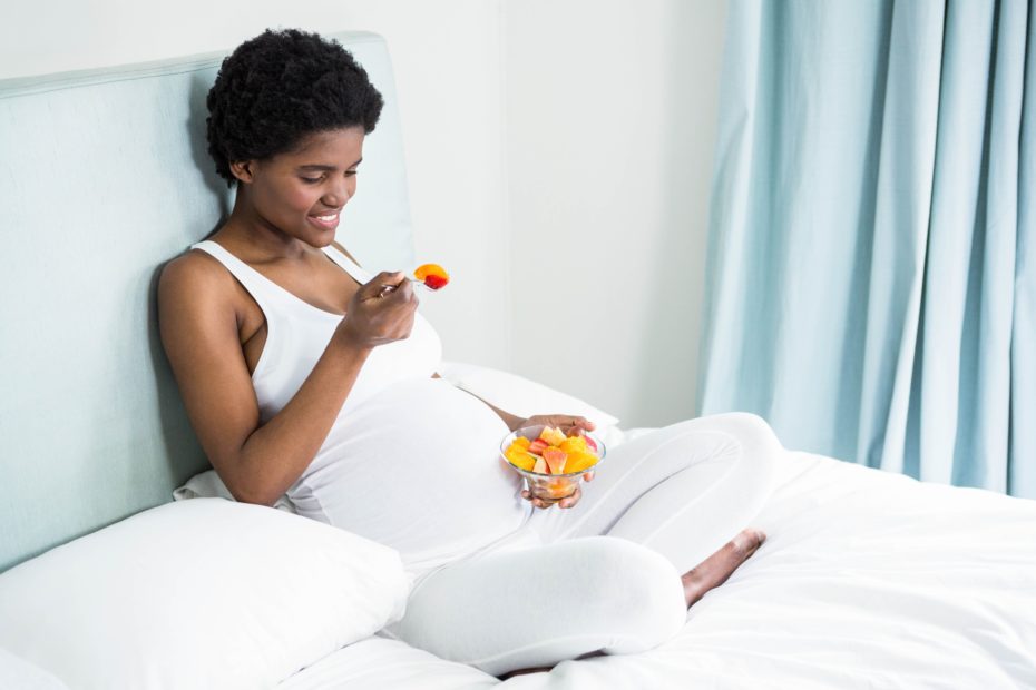 mulher comendo alimentos fontes de ferro na gravidez sentada na cama