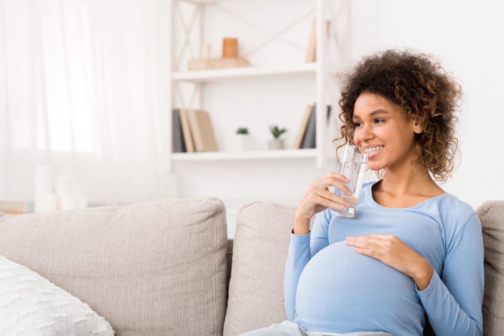 mulher grávida sentada em sofá bebendo água