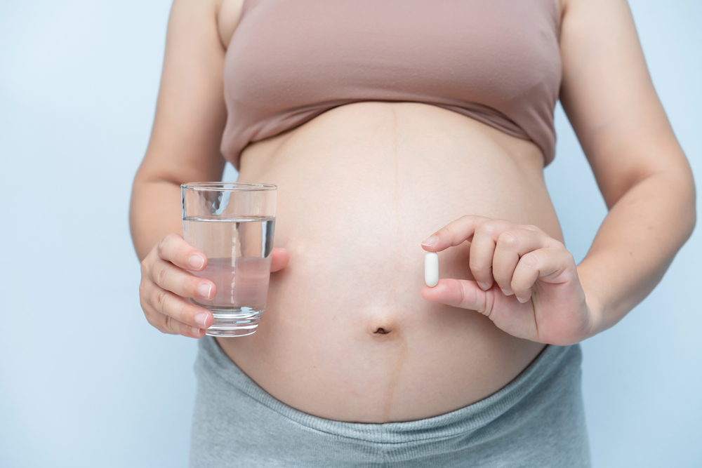 grávida segurando uma cápsula de vitamina e um copo de água